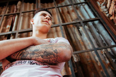 Low angle view of young man standing by corrugated iron