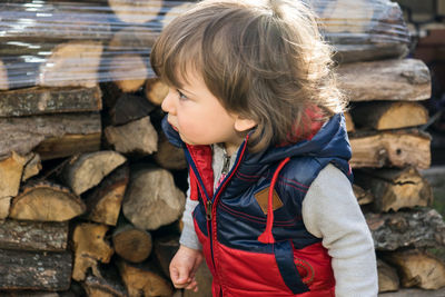 Cute boy looking away while standing against stacked firewood