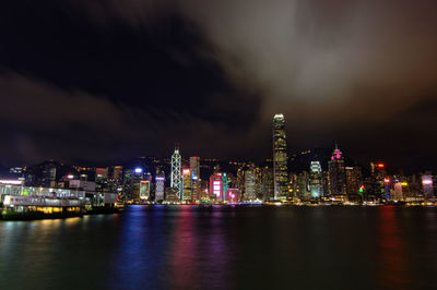 Illuminated buildings by river against sky at night