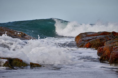 Waves splashing on rocks at shore against sky