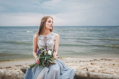 Beautiful young woman at beach against sky