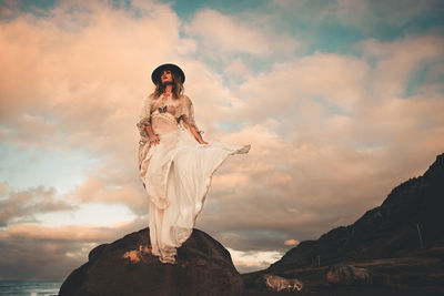 Woman standing on rock by sea against sky during sunset