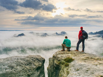 Hiker and photo enthusiast stay with tripod on cliff. peak with two men taking photos in autumn day