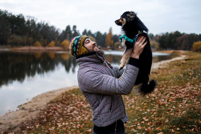 Bearded man with his dog playing in autumn park near lake.