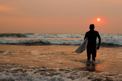 Rear view of man standing on beach during sunset