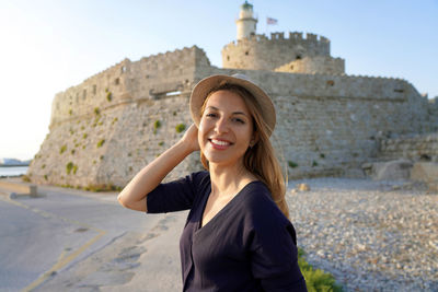 Portrait of young tourist woman in rhodes island with the tower and fort of saint nicholas, greece