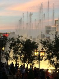 Silhouette trees by illuminated city against sky during sunset