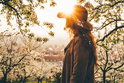 Back view of girl in hat standing in park in evening sunset. 