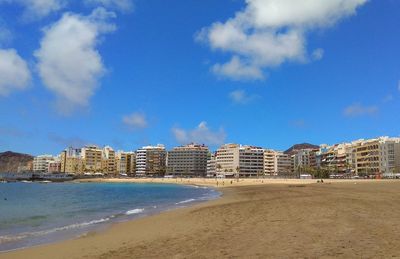 Buildings by sea against blue sky