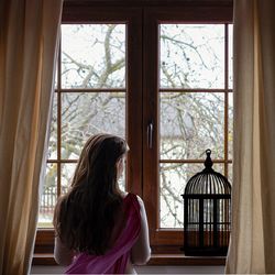 A back of a woman looking out through a windo.