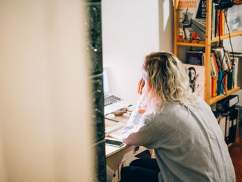 Side view of woman sitting and studying by laptop in living room