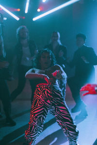 Young woman bending backwards while dancing against friends at nightclub enjoying weekend