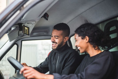 Smiling male mover showing mobile phone to coworker while sitting in truck