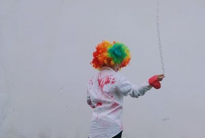 Low angle view of boy wearing costume swinging chain standing against wall