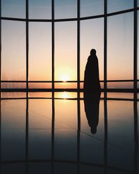 Silhouette person standing on floor by glass window during sunlight