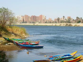 Boats moored on sea by city against sky