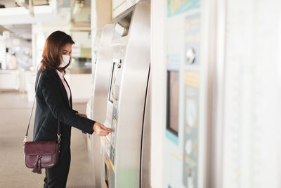 Businesswoman wearing mask using ticket machine