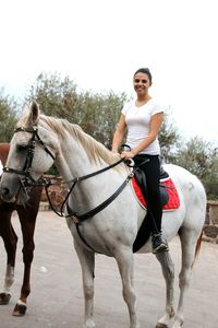 Full length of smiling young woman riding horse