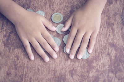 Cropped hands of child holding coins on table