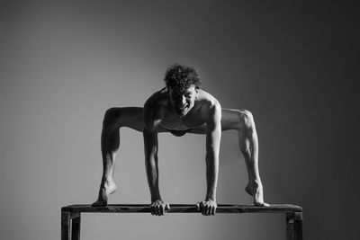 Portrait of shirtless man exercising on bench against wall