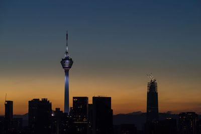 Communications tower in city against sky during sunset