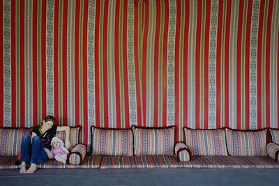 Smiling woman with doll on seat against patterned wall