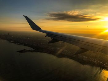 Airplane flying over sea against sky during sunset