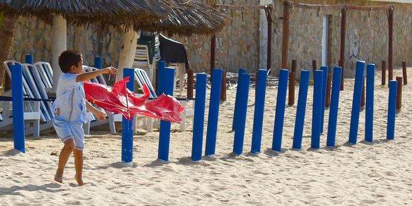 Boy with red kite by blue wooden posts at beach during sunny day