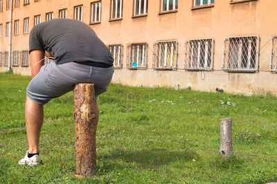 Rear view of man sitting on wooden post against building
