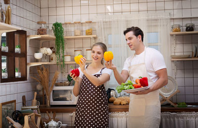 Couple holding vegetables while standing in kitchen