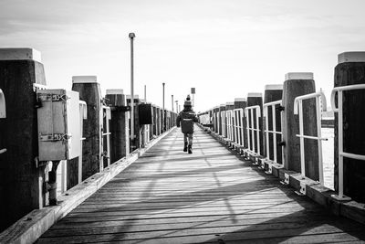 Rear view of boy walking on pier over river