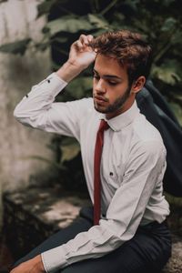 Young man looking away while sitting outdoors