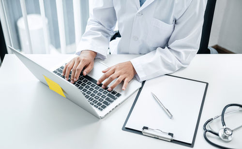 Midsection of doctor using laptop at clinic