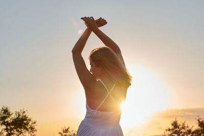 A young woman raises her arms at sunset. concept of freedom