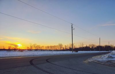 Snow covered road against sky during sunset