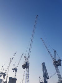 Low angle view of cranes against clear blue sky