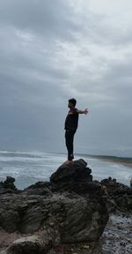 Man standing on rock by sea against sky