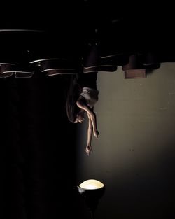 Upside down image of woman reaching for illuminated lamp against wall