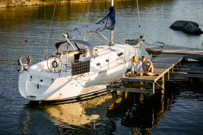 High angle view of couple working over laptop while sitting on jetty by yacht over lake during summer vacation