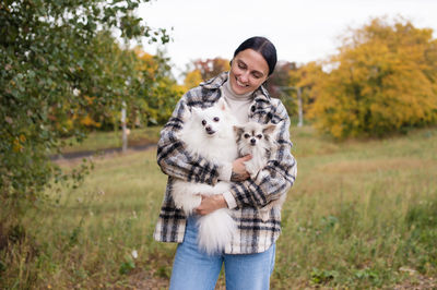 A cute girl holds her pets a white pomeranian and a chihuahua in the autumn forest