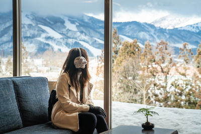 Woman looking at mountains through window while sitting on sofa 