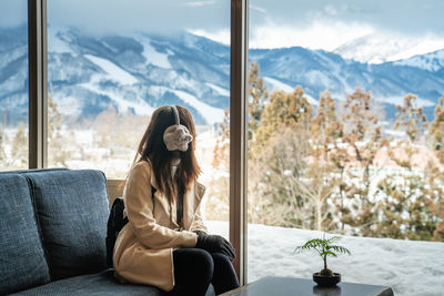 Woman looking at mountains through window while sitting on sofa 