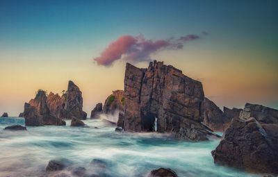 Rock formations by sea against sky during sunset