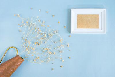 Directly above shot of blank picture frame with flower vase on blue background