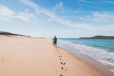 Rear view of woman walking at beach against sky