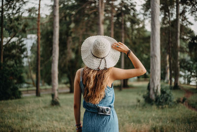 Woman wearing hat while standing on grass in forest