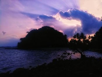 Silhouette trees by sea against sky at sunset