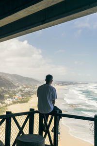 Rear view of man sitting on railing against sea