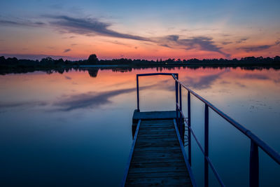 Jetty with a handrail on the lake, horizon and evening colorful clouds on the blue sky