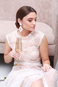 Side view of young woman holding bottle while sitting on sofa at home